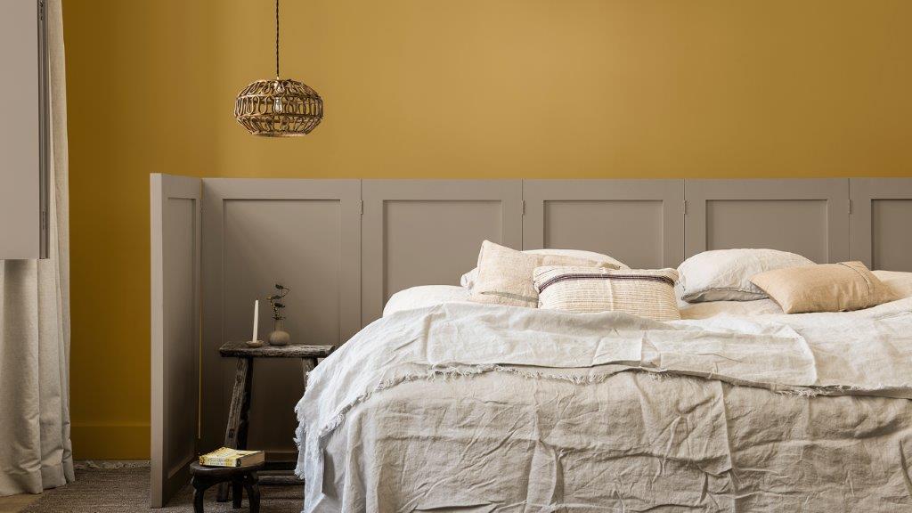 Bedroom wall painted in golden yellow and Brave Ground, with paneled screen behind bed Dulux_CF21_Év_színe_Időtlen_paletta_magyar_2